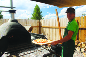 Noah Ronczkowski poses with a Caldera pizza before sliding it into the restaurant’s hand-built oven.