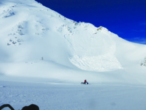 A snowmobiler rides beneath a recent avalanche, giving other slopes with the potential to slide a wide berth. 
