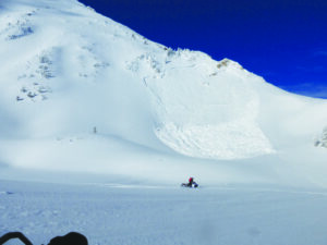 A snowmobiler rides beneath a recent avalanche, giving other slopes with the potential to slide a wide berth.