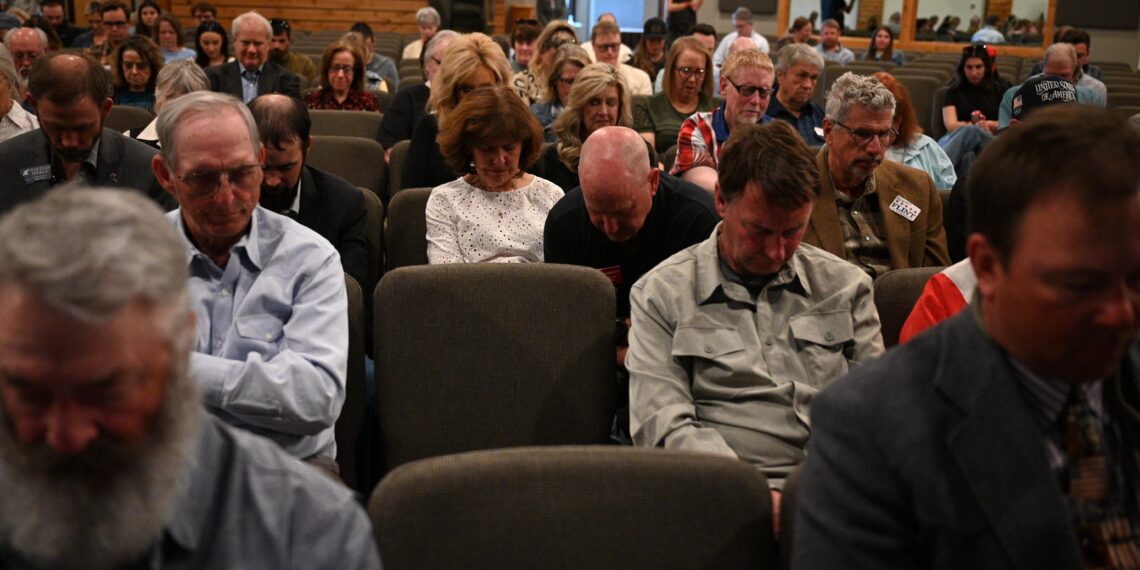 Crowded auditorium of adults seated in rows, many looking down at the event.",