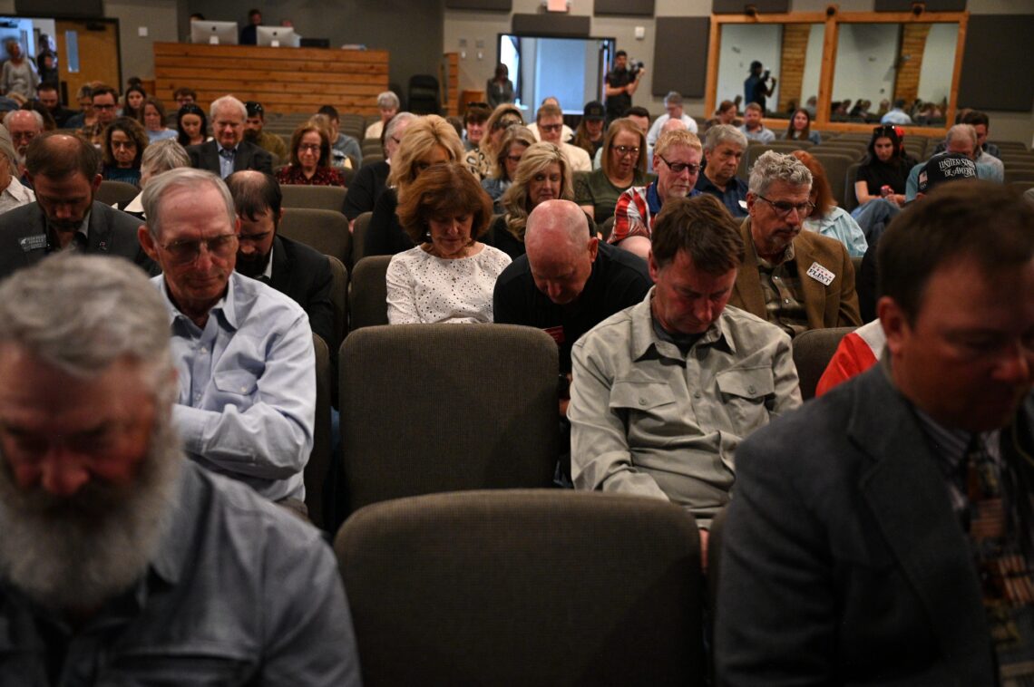 Crowded auditorium of adults seated in rows, many looking down at the event.",