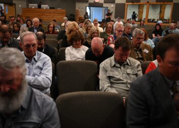 Crowded auditorium of adults seated in rows, many looking down at the event.",