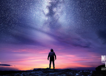 A person silhouetted on rocky ground gazing at a vibrant sunset and the Milky Way across a starry sky, with venue branding bottom right.