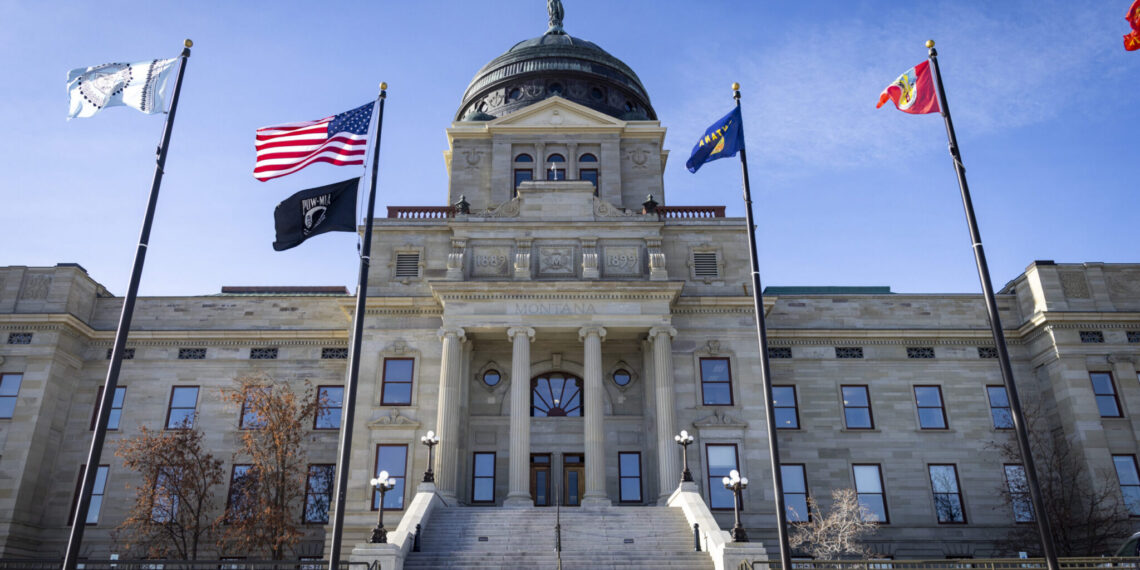 Montana Capitol building with a domed roof, grand columns, and flagpoles flying US and state flags in front of a stone facade.