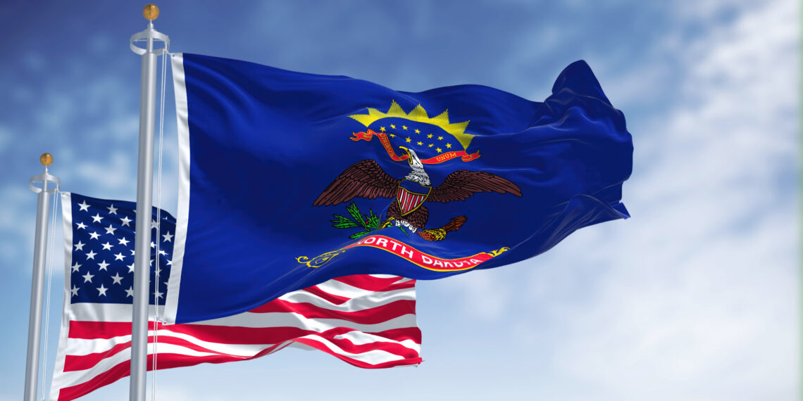 Blue North Dakota state flag with the Great Seal and eagle, waving beside an American flag in a clear sky.