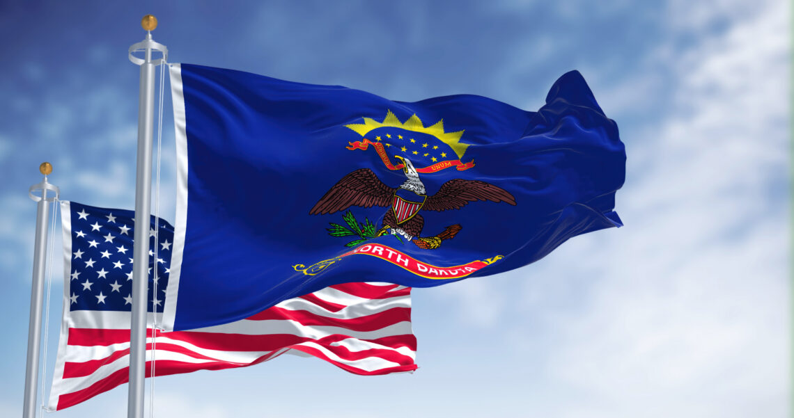 Blue North Dakota state flag with the Great Seal and eagle, waving beside an American flag in a clear sky.