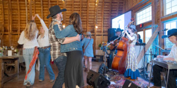 Couple dancing closely in a rustic wooden hall while a band plays nearby on stage.