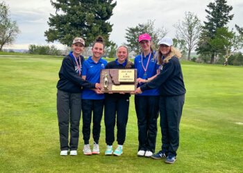 Five young athletes pose with a large trophy plaque outdoors on a grassy field, wearing blue and dark athletic outfits and medals.