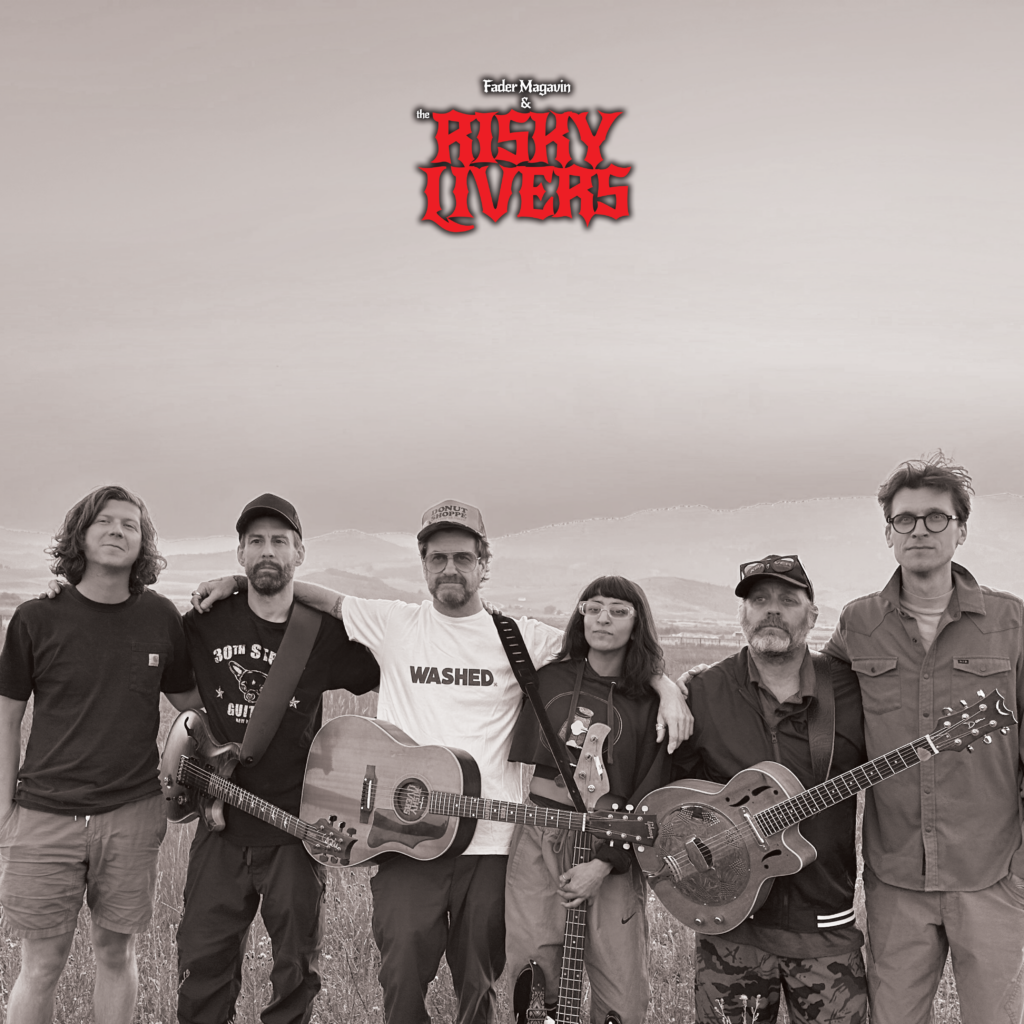 Eight musicians stand arm-in-arm in a grassy field, each holding or wearing a guitar, posing for an outdoor band photo in monochrome.