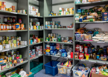 Shelves in a pantry stocked with canned goods and packets, labeled Pasta sauce, Vegetables, Rice, and Pasta.