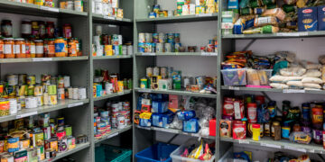 Shelves in a pantry stocked with canned goods and packets, labeled Pasta sauce, Vegetables, Rice, and Pasta.