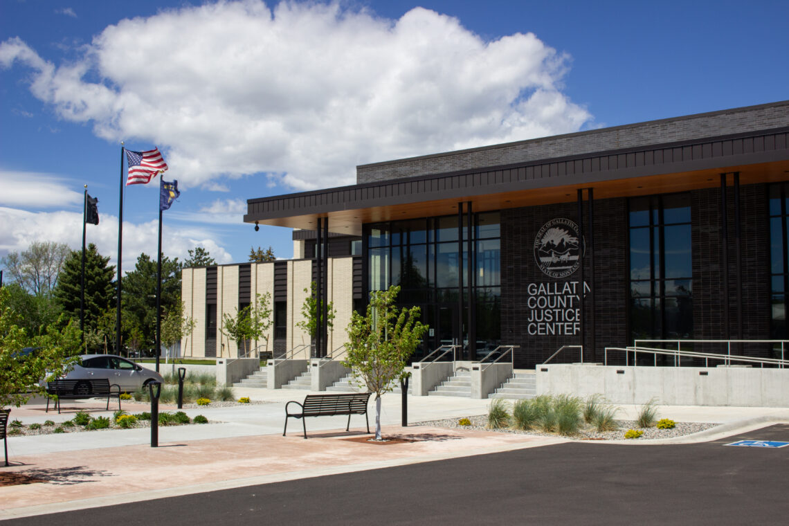 Exterior view of Gallatin County Justice Center with American and state flags, glass entrance, and landscaped plaza.