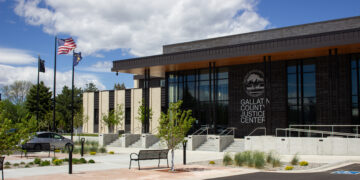Exterior view of Gallatin County Justice Center with American and state flags, glass entrance, and landscaped plaza.