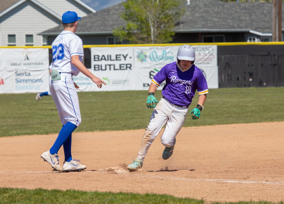 Two baseball players near a base: one in a white uniform with blue cap approaching a bag, the other in purple Rangers jersey sliding toward home plate.