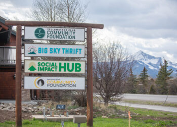 Signpost with multiple community organization signs against mountain backdrop (Big Sky Thrift, Community Foundation, Social Hub)