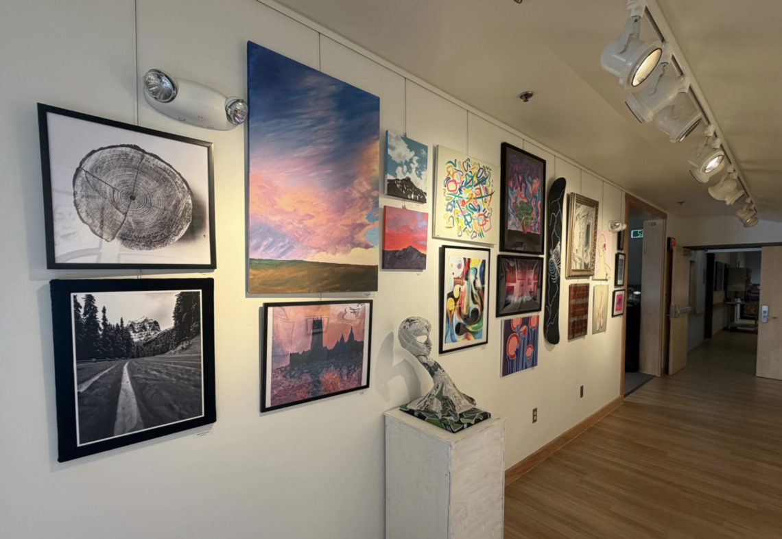 Gallery wall of assorted framed art along a well-lit hallway with wooden floor and track lighting above.