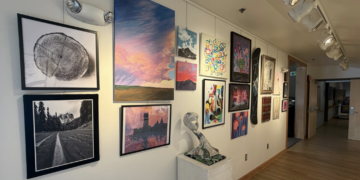Gallery wall of assorted framed art along a well-lit hallway with wooden floor and track lighting above.