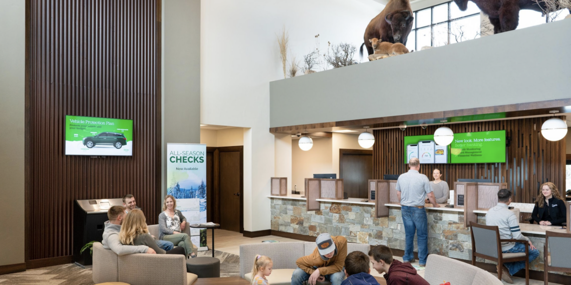 Modern bank lobby with seating areas and customers at service desks, plus buffalo statues visible on an upper level.