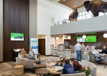 Modern bank lobby with seating areas and customers at service desks, plus buffalo statues visible on an upper level.