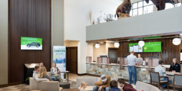 Modern bank lobby with seating areas and customers at service desks, plus buffalo statues visible on an upper level.