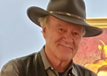 Smiling older man wearing a wide-brimmed hat and gray shirt.