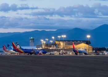 Southwest airplanes parked at a small airport terminal with a control tower and mountain backdrop at dusk.