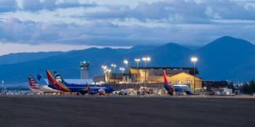 Southwest airplanes parked at a small airport terminal with a control tower and mountain backdrop at dusk.