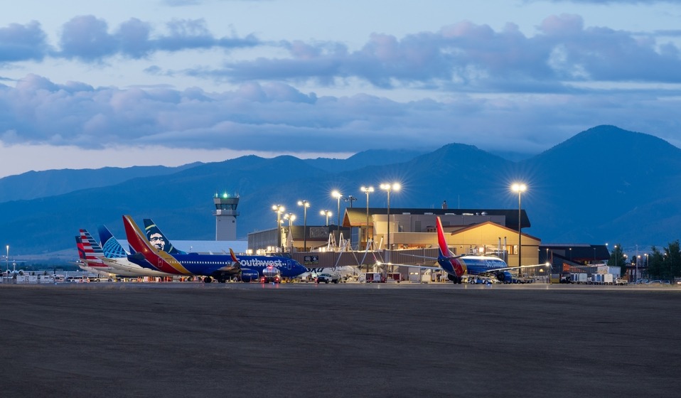 Southwest airplanes parked at a small airport terminal with a control tower and mountain backdrop at dusk.
