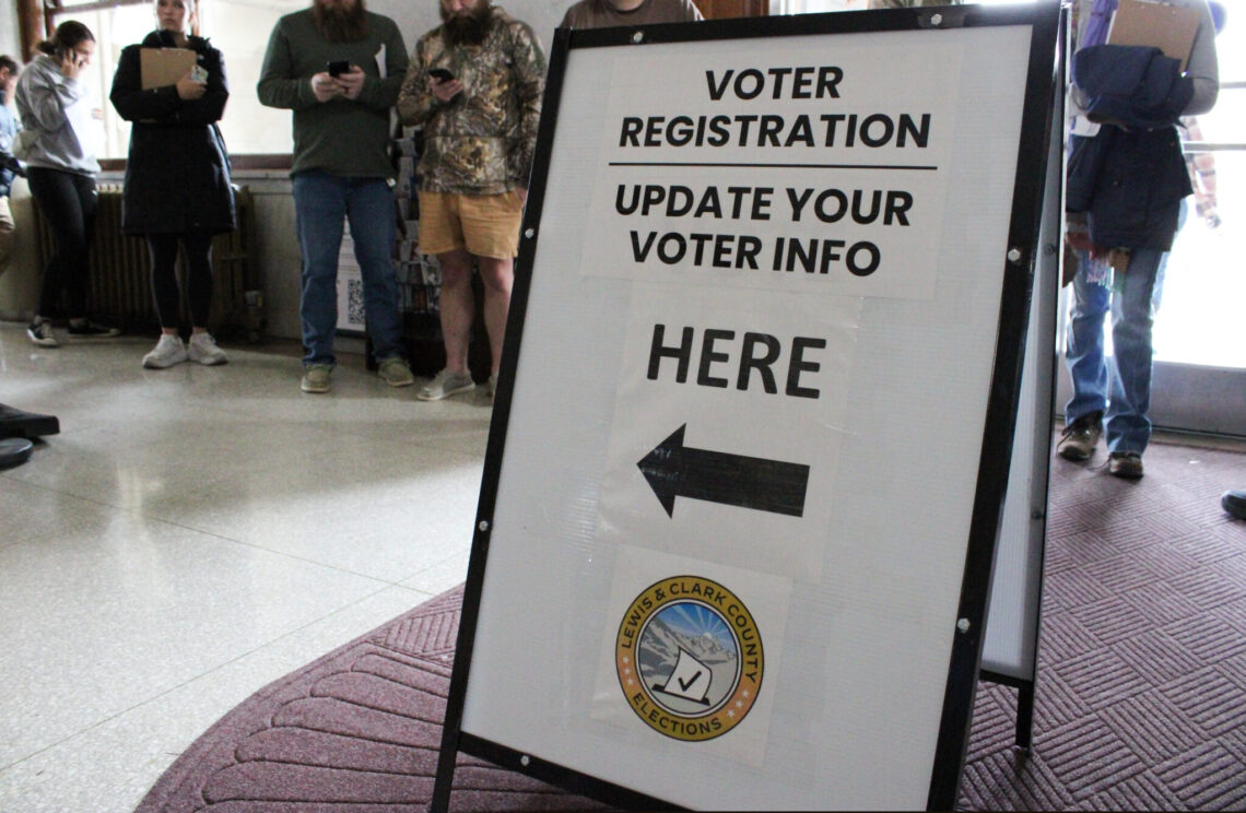 Bold voter registration sign in a public space reading 'Voter Registration Update Your Voter Info Here' with a left-pointing arrow and county seal visible below.
