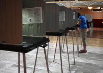 Voter at a privacy voting booth row in a polling place with gray dividers.
