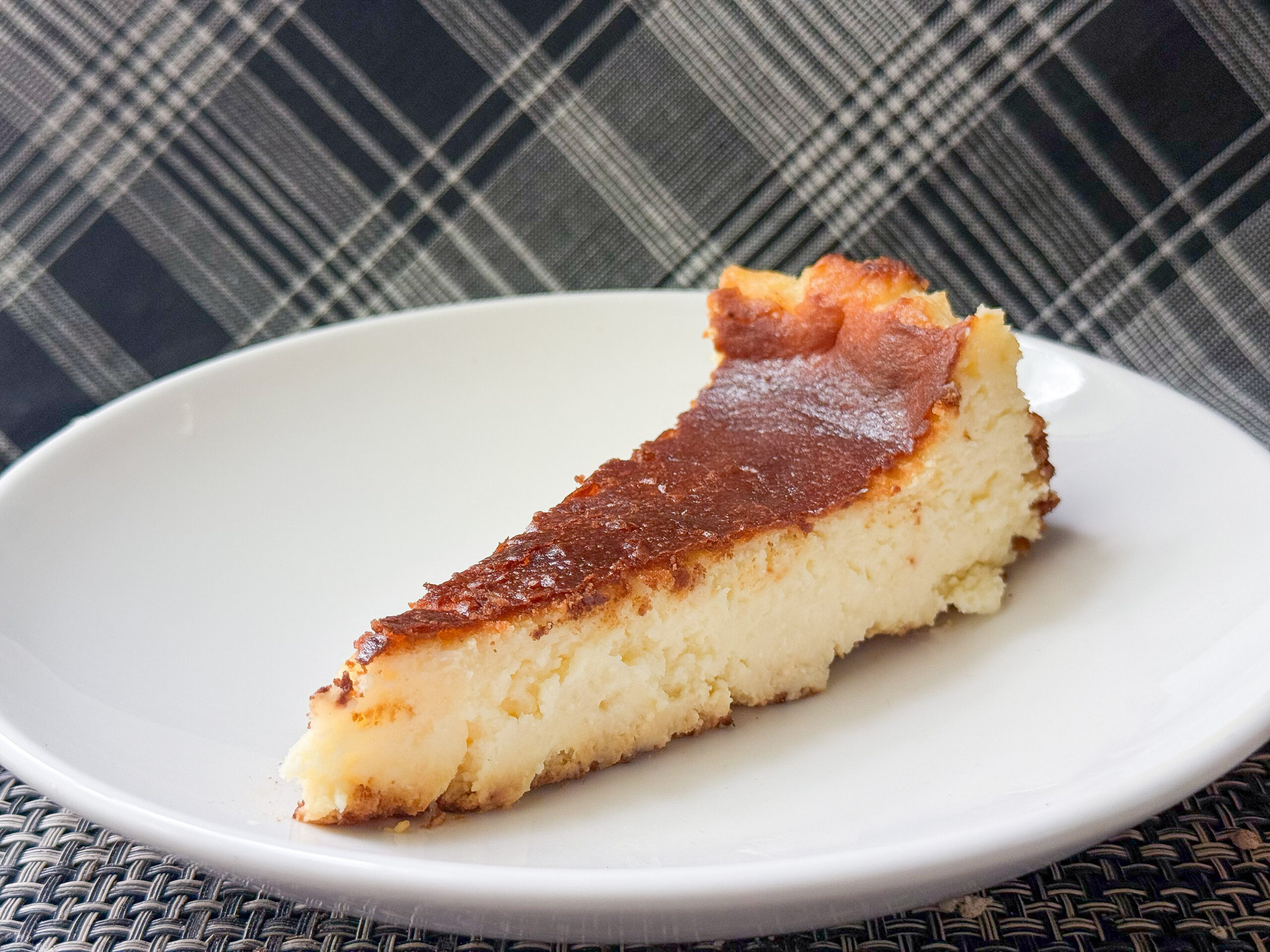 Slice of baked pie on a white plate, showing a golden-brown crust and pale yellow filling, with a plaid tablecloth in the background.