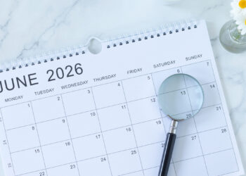 Open June 2026 calendar page on a marble desk with a cup of coffee, a small vase of daisies, and a magnifying glass nearby.