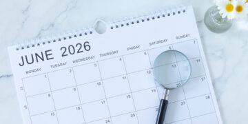 Open June 2026 calendar page on a marble desk with a cup of coffee, a small vase of daisies, and a magnifying glass nearby.