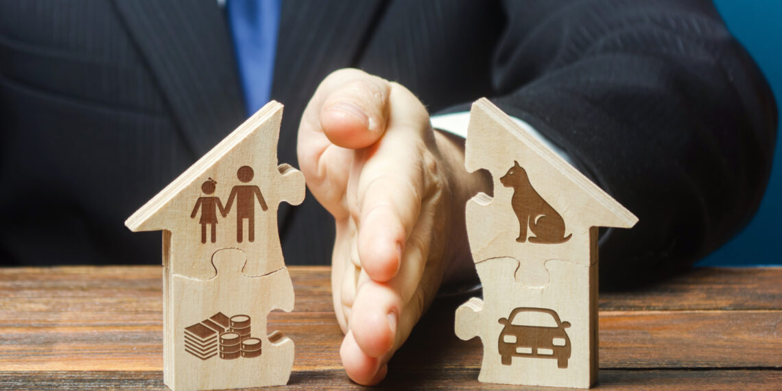 Hands pressing together two wooden house-shaped puzzle pieces, one with a family icon and coins, the other with a car icon, symbolizing family, housing, and financial planning.