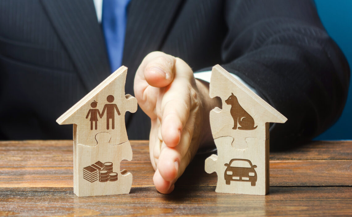 Hands pressing together two wooden house-shaped puzzle pieces, one with a family icon and coins, the other with a car icon, symbolizing family, housing, and financial planning.