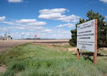 Roadside sign for Great Falls Agri-Tech Park in a rural lot with a blue sky and wispy clouds, foreground grass.