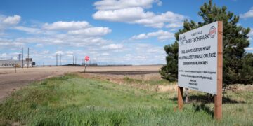 Roadside sign for Great Falls Agri-Tech Park in a rural lot with a blue sky and wispy clouds, foreground grass.