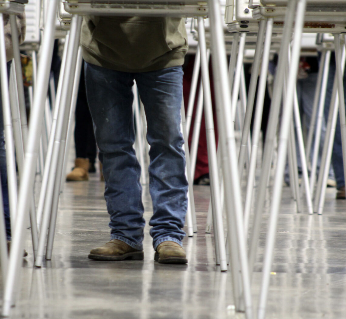 Person in blue jeans and brown boots walking between rows of folding tables with metal legs.