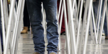 Person in blue jeans and brown boots walking between rows of folding tables with metal legs.