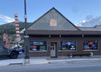 Front view of Carmel's Bar & Grill building with neon signs in the windows and a tall vertical 'CARMEL'S' sign on the left against a blue sky.
