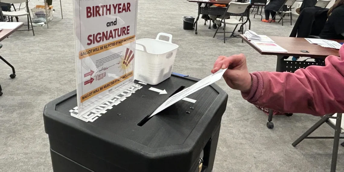 Voter inserts a ballot into a ballot drop box at a polling station.”