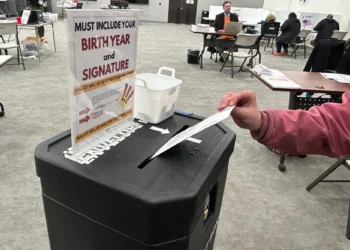 Voter inserts a ballot into a ballot drop box at a polling station.”