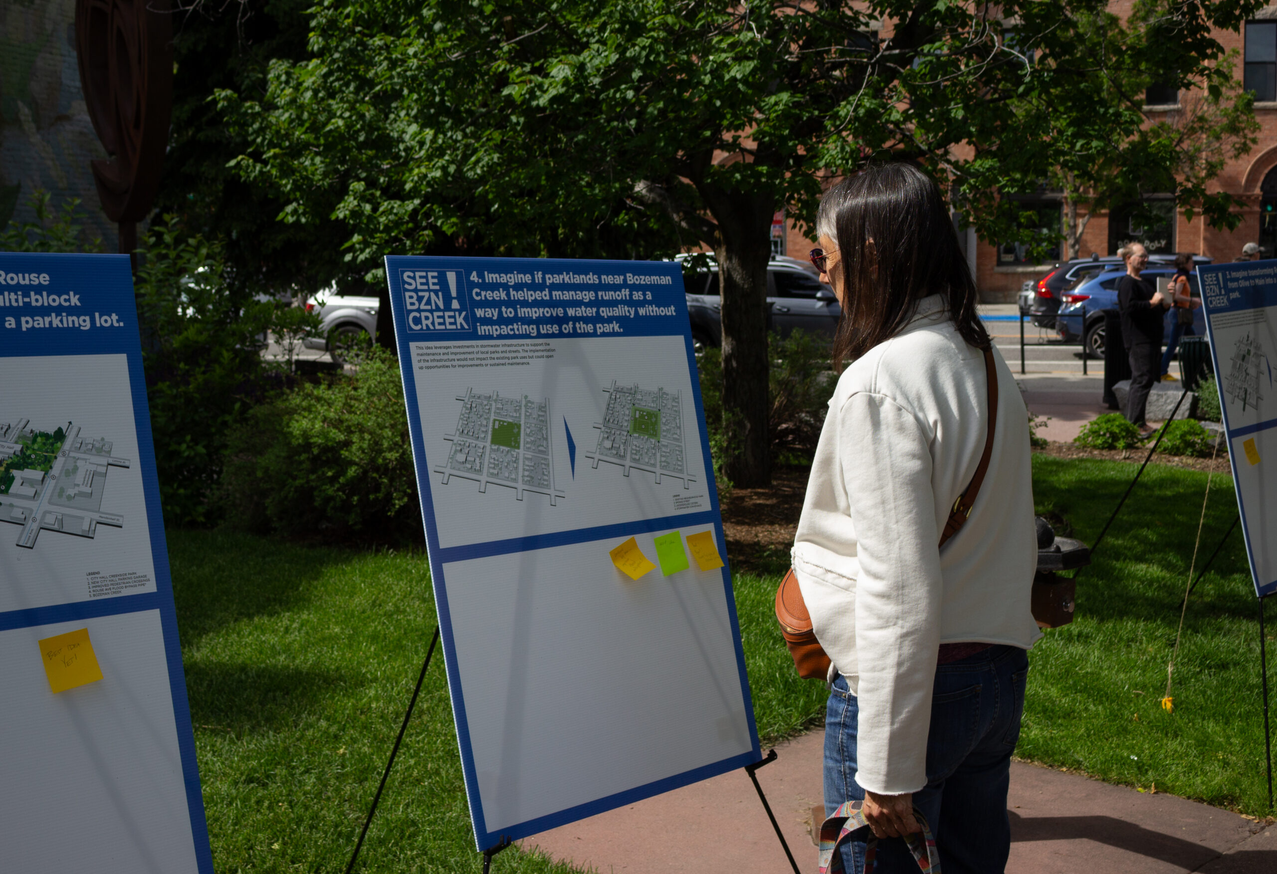 Person in a white jacket reads an outdoor information board with maps in a park setting