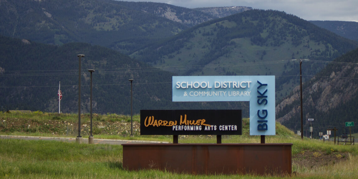 Signs for a school district and community library with distant mountains in the background.