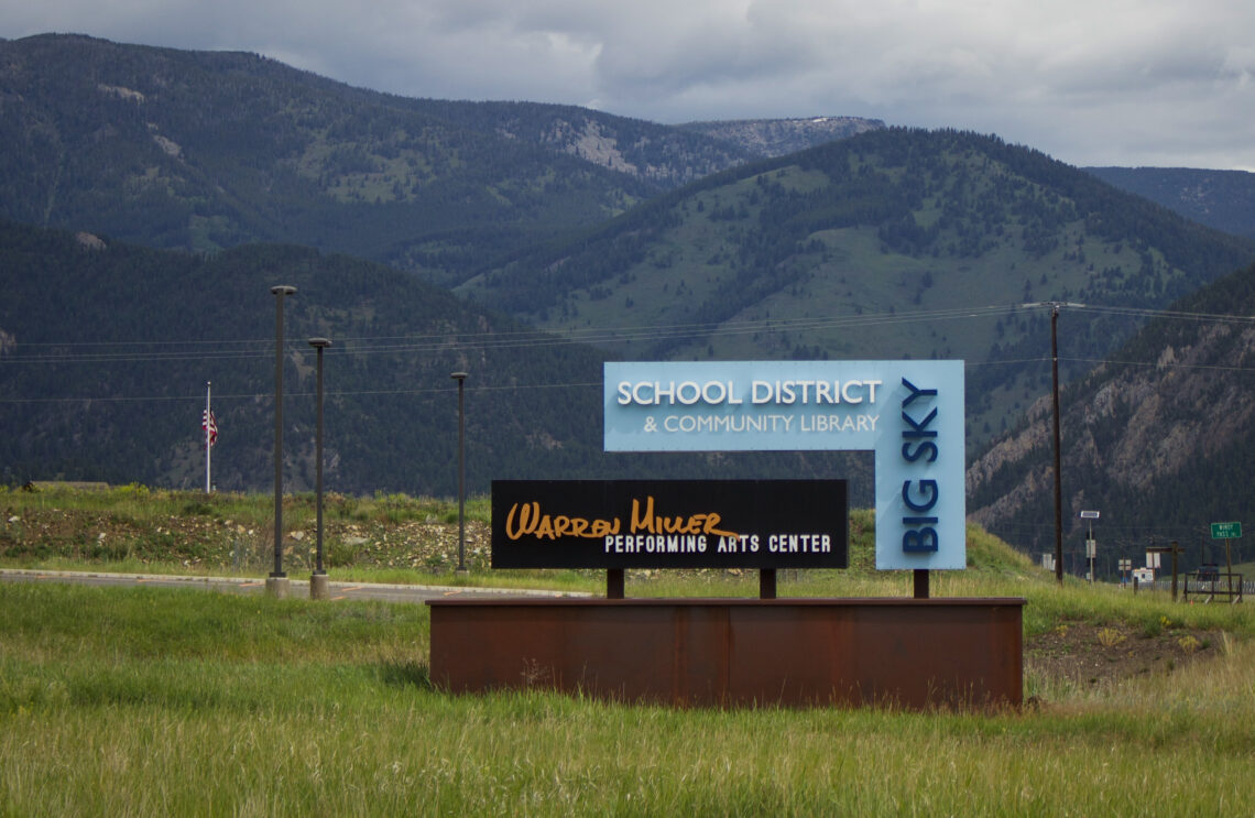 Signs for a school district and community library with distant mountains in the background.