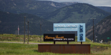 Signs for a school district and community library with distant mountains in the background.
