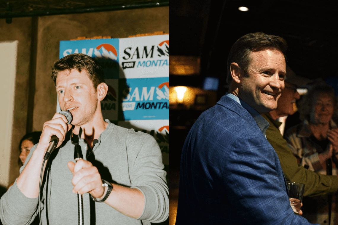 Two men at an event: the left man speaks into a microphone in front of campaign boards, while the man on the right smiles in a blue suit and holds a glass.