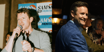 Two men at an event: the left man speaks into a microphone in front of campaign boards, while the man on the right smiles in a blue suit and holds a glass.