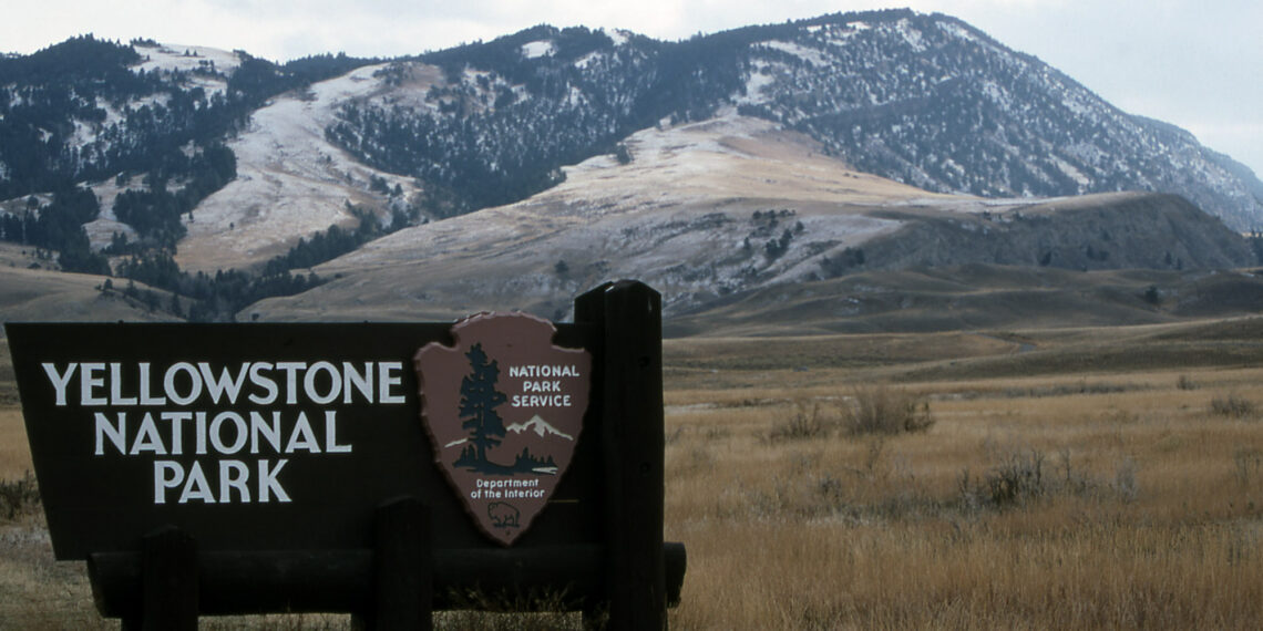 Sign for Yellowstone National Park with snow-dusted mountains in the background.