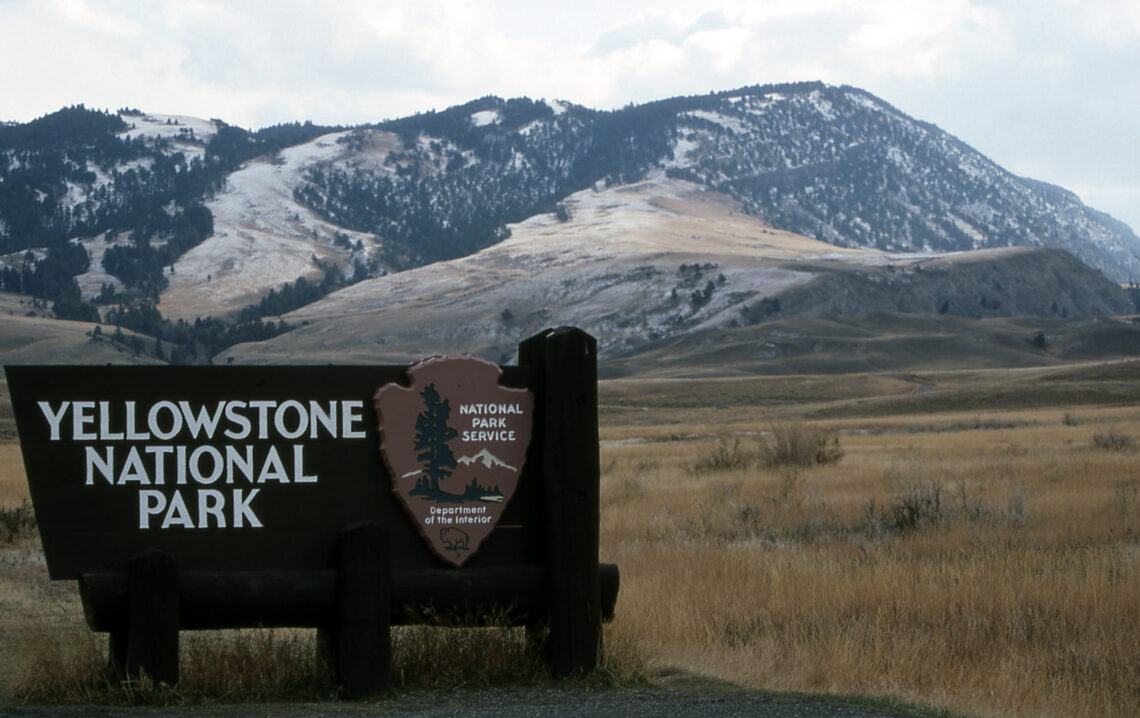 Sign for Yellowstone National Park with snow-dusted mountains in the background.